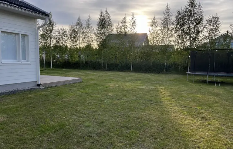 Oululainen takapiha ennen: laaja avoin nurmi, kalustamaton terassilaituri ja trampoliini