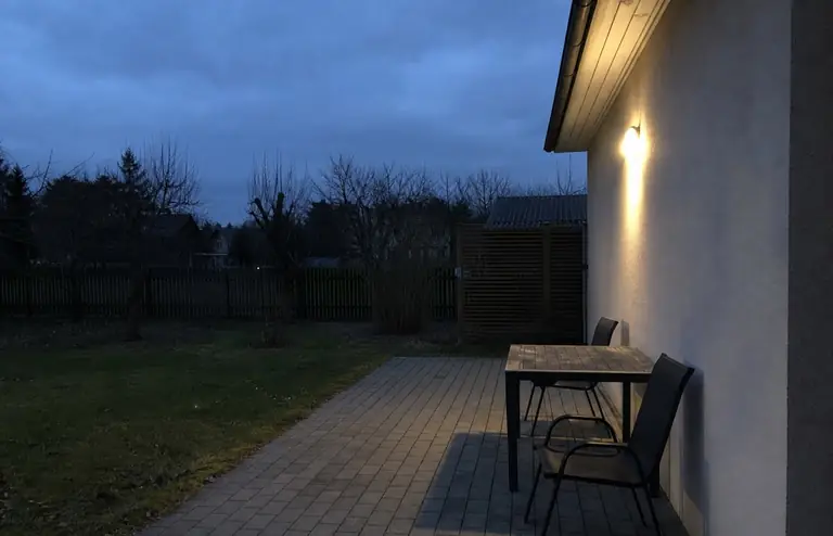 Terrass õhtul enne: üks ere seinalamp ja tühi laud